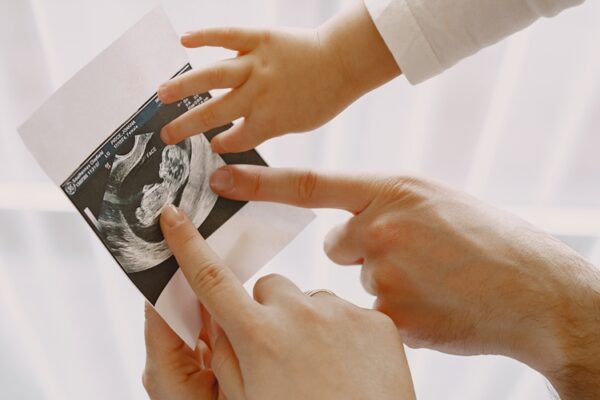 Pregnant mom dad and little daughter look at photo Mom dad and daughter watching photos. Family in light clothes. Family expecting a baby.